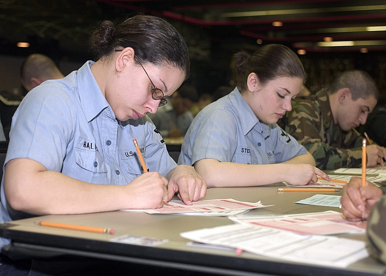 Test takers in a large room filling in paper answer sheets with yellow number 2 pencils
